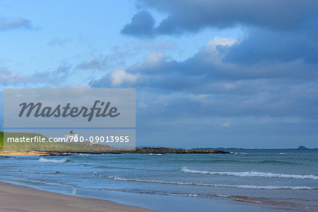 Beach along the North Sea in Bamburgh with the Bamburgh Lighthouse in the distance in Northumberland, England, United Kingdom