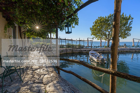 Sun shining on the stone patio at Locanda San Vigilio overlooking a little harbor and Lake Garda in the morning at Punta San Vigilio in Garda, Veneto, Italy Sun shining on the stone patio at Locanda San Vigilio overlooking a little harbor and Lake Garda in the morning at Punta San Vigilio in Garda, Veneto, Italy