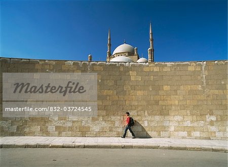 Tourist walking past large wall with Mohammed Ali Mosque behind in Citadel of Cairo