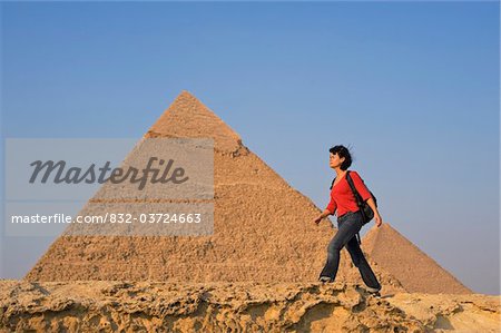 Woman with rucksack walking along ancient wall in front of Pyramids