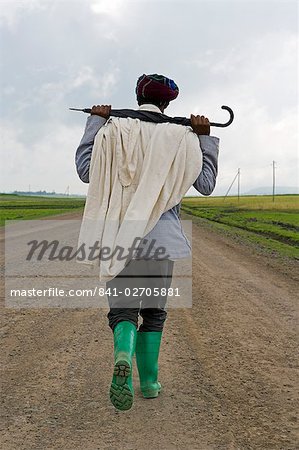 Man walking along the road during the rainy season wearing green boots and holding an umbrella, The Ethiopian Highlands, Ethiopia, Africa
