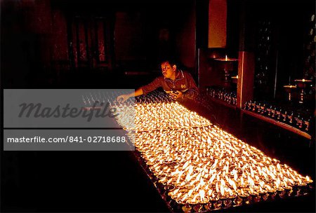 Man lights butter lamps in the early morning inside the Buddhist Deva Dharma Mahavihar temple on the edge of Swayambhunath (Swayambhu) (Monkey Temple) stupa on a hill above Kathmandu, Nepal, Asia