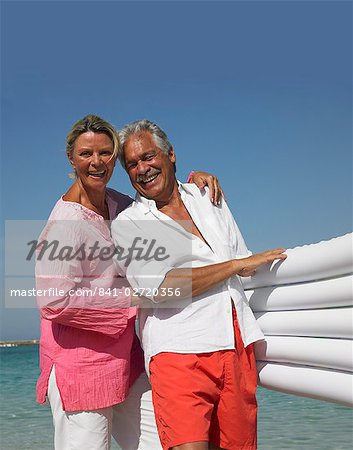 Senior couple on beach holding an air bed