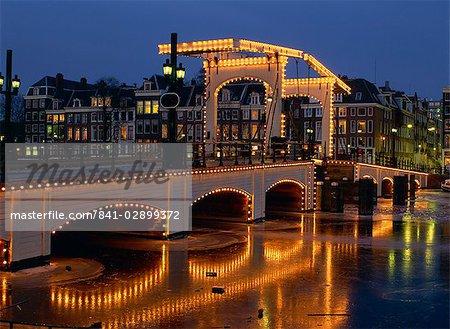 Lights on the Magere Brug (Skinny Bridge) reflected in the canal, in winter in Amsterdam, Holland, Europe