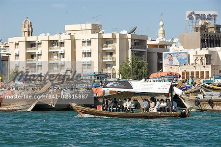 Abra (cross-creek ferry) chugs past dhow wharves and modern buildings of Deira, Dubai Creek, Dubai, United Arab Emirates, Middle East