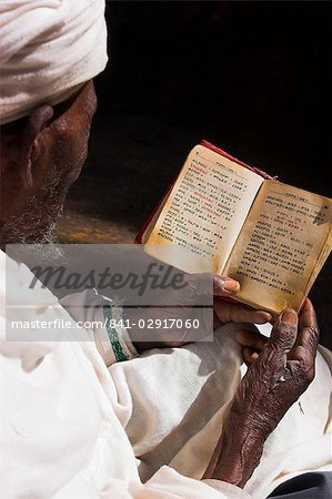 Old man wearing traditional gabi (white shawl) reading Holy Bible in rock-hewn monolithic church of Bet Medhane Alem (Saviour of the World), Lalibela, Ethiopia, Africa