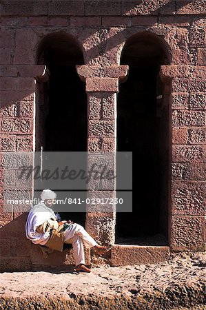 Pilgrim sits in early morning sun reading his Holy Bible at entrance doors to Bet Maryam church (St. Mary's), believed to be the oldest rock hewn church in Lalibela, UNESCO World Heritage Site, Lalibela, Ethiopia, Africa