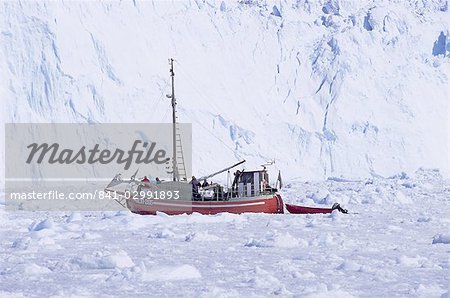 Red wooden boat crossing the ice in front of the Eqi Glacier, near Ilulissat, Greenland, Polar Regions