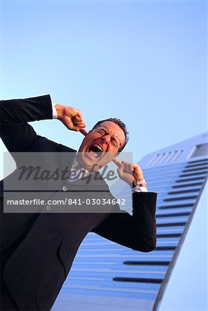 Business man with fingers in his ears,outdoors,shouting