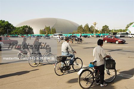 The National Theatre designed by the French architect Paul Andreu, and cyclists commuting in central Beijing, Beijing, China, Asia