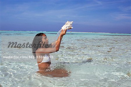 Young woman in the sea holding up a shell, Los Roques, Venezuela, South America