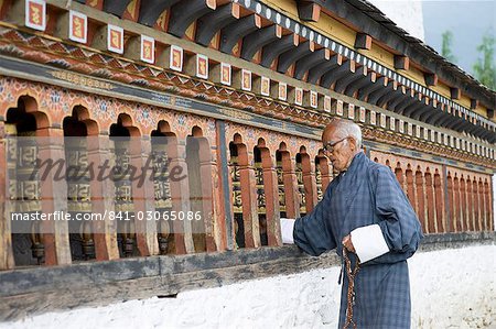 Old Bhutanese man turning prayer wheels in Buddhist temple, Thimphu, Bhutan, Asia