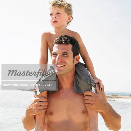 Son (6-8) sitting on father's shoulders on beach