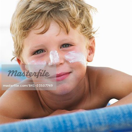 Boy (6-8) on beach with suncream on face