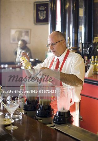 Barman making cocktails in El Floridita, a bar frequented by author Ernest Hemingway whose lifesize bronze statue is visible in the background, Havana, Cuba, West Indies, Caribbean, Central America