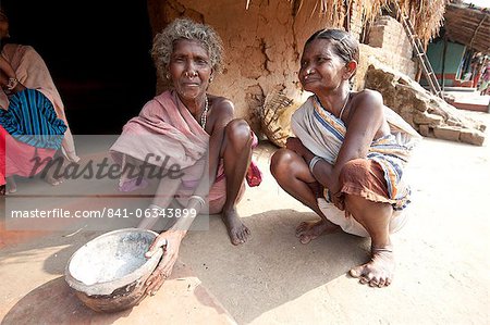 Two Desia Kondh tribal women squatting outside their village house holding welcome bowl of ash, Bissam Cuttack, Orissa, India, Asia