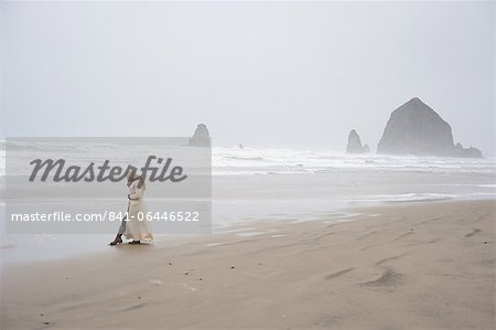 Woman talks on phone with Haystack Rock in the distance at popular tourist destination, Cannon Beach, Oregon, United States of America, North America