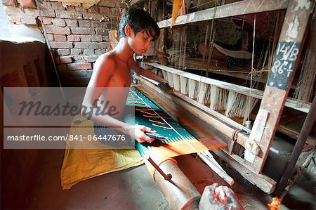 Young boy at domestic loom weaving patterned silk sari using several spools of silk, Vaidyanathpur weaving village, Orissa, India, Asia