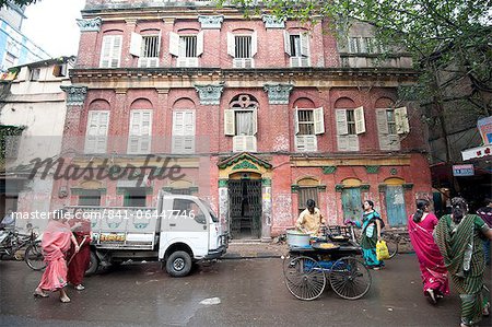 Street snack seller with his wheeled stall outside beautiful old Raj era building in Kolkata back street, West Bengal, India, Asia