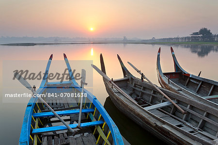 Traditional rowing boat moored on the edge of flat calm Taungthaman Lake at dawn with the colours of the sky reflecting in the calm water, close to the famous U Bein teak bridge, near Mandalay, Myanmar (Burma), Asia