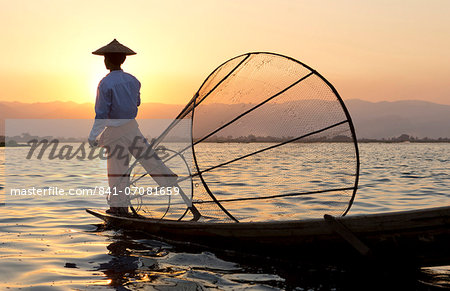 Intha 'leg rowing' fishermen at sunset on Inle Lake who row traditional wooden boats using their leg and fish using nets stretched over conical bamboo frames, Inle Lake, Myanmar (Burma), Southeast Asia