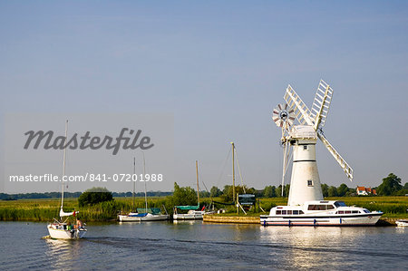 Sailing boats and river cruisers pass windmill on Norfolk Broads, United Kingdom