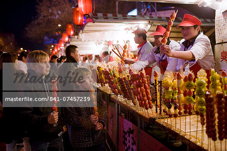 Boys eat candied strawberry sticks from stall in the Night Market, Wangfujing Street, Beijing, China