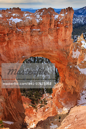 Red-hued limestone arch lit by morning sun with snow in winter at Natural Bridge, Bryce Canyon National Park, Utah, United States of America, North America