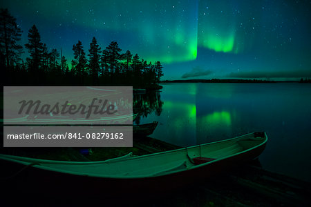 Beached canoes and Aurora Borealis and stars reflected in lake at night, Muonio, Lapland, Finland, Scandinavia, Europe