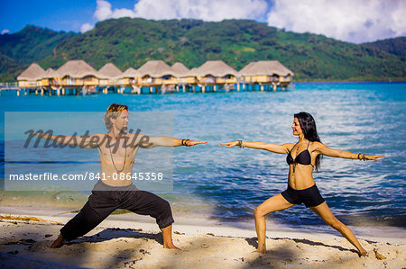 Couple doing yoga in front of overwater bungalows, Le Taha'a Resort, Tahiti, French Polynesia, South Pacific, Pacific