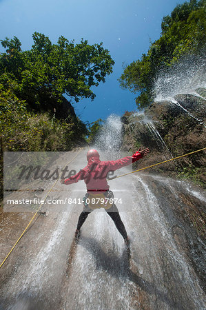 A man pauses to hold his arms in the falling water while canyoning, Nepal, Asia