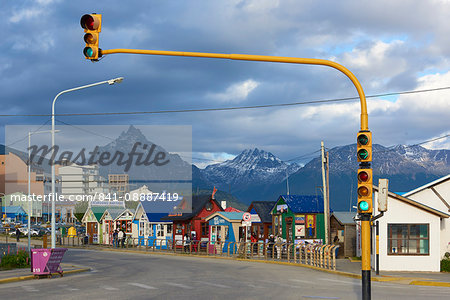 Colourful houses on touristic road framed by traffic lights post with snowy mountain chain beyond, Ushuaia, Argentina, South America