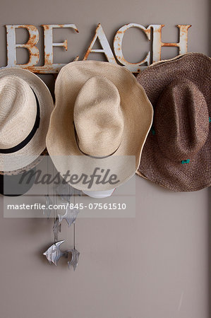 Rusty beach named hat rack with straw beach hats and silver fish wind chime in South African beach house