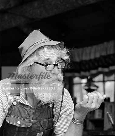 1970s OLDER MAN HILLBILLY CHARACTER WEARING CLOTH HAT OVERALLS GINGHAM SHIRT WITH GLASSES BEARD OUTDOOR