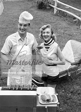 1950s COUPLE BACKYARD GRILL COOK HOT DOGS MAN WEARING APRON TOQUE & SKEWERED HOT DOG