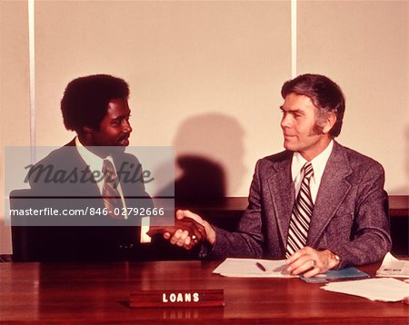 1970s AFRICAN AMERICAN MAN SHAKING HANDS WITH BANK LOAN OFFICER