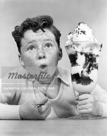 1950s FRECKLE FACED BOY WITH FUNNY EXPRESSION LOOKING AT GIANT SIZED ICE CREAM SUNDAE PARFAIT