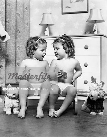 1950s TWIN GIRLS SITTING IN A DOUBLE SEAT WEARING PANTIES ONLY WHILE EATING GRAHAM CRACKERS