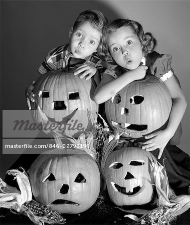 1950s BOY AND GIRL STANDING BEHIND AND OR HOLDING FOUR JACK-O-LANTERNS WITH INDIAN CORN MAKING SPOOKY FACES