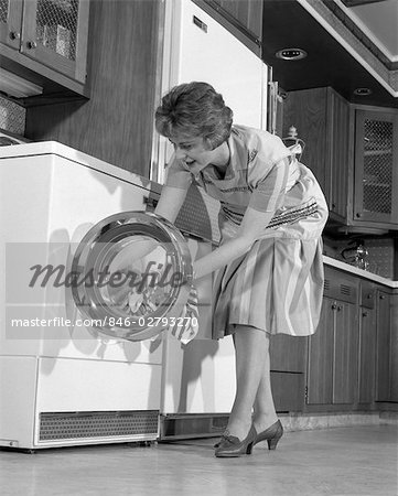 1960s HOUSEWIFE IN KITCHEN PUTTING LAUNDRY INTO WASHER