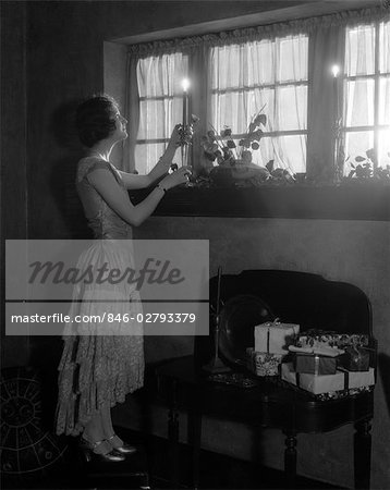 1920s WOMAN PARTY DRESS RUFFLES ON SKIRT PLACING A LIGHTED CANDLE IN WINDOW GIFTS PRESENTS WRAPPED ON SIDE