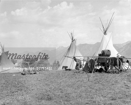 1920s 1930s NATIVE AMERICAN INDIAN CAMP VILLAGE TIPI TEEPEE WAGONS MOUNTAINS IN BACKGROUND KOOTENAI INDIANS BRITISH COLUMBIA