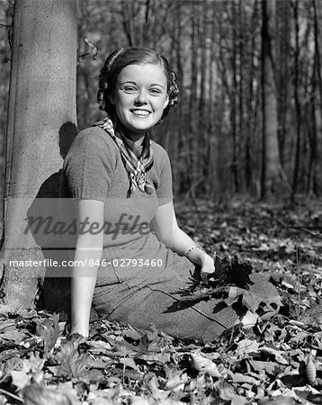 1940s PRETTY SMILING TEEN YOUNG WOMAN GIRL SITTING UNDER TREE IN AUTUMN LEAVES PORTRAIT