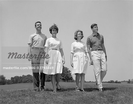 1960s TWO TEENAGE COUPLES BOYS GIRLS FULL LENGTH WALKING THROUGH FIELD TOWARDS CAMERA