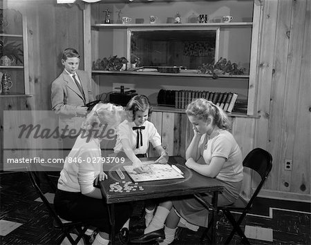 1950s GIRLS PLAYING SCRABBLE IN REC ROOM WITH BOY CHANGING RECORDS 1950s GIRLS PLAYING SCRABBLE IN REC ROOM WITH BOY CHANGING RECORDS