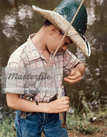 1920s 1930s FARM BOY WEARING STRAW HAT AND OVERALLS SITTING ON LOG