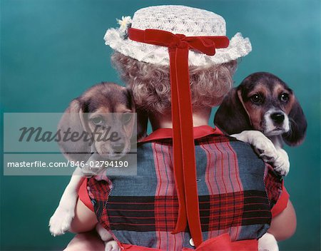 CLOSE-UP REARVIEW OF LITTLE GIRL WITH STRAW HAT HOLDING TWO BEAGLE PUPPIES 1950s STUDIO
