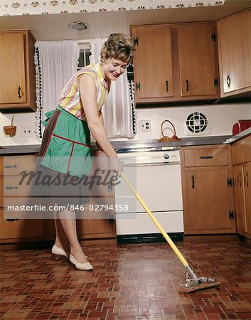 1960s WOMAN IN APRON CLEANING KITCHEN FLOOR WITH SPONGE MOP