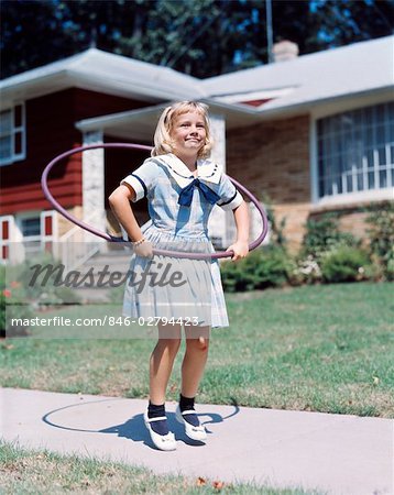 1950s 1960s YOUNG BLOND GIRL PLAYING WITH HULA HOOP OUTSIDE ON SUBURBAN SIDEWALK IN SAILOR STYLE DRESS