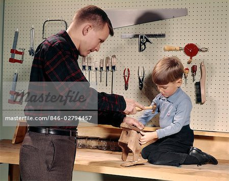 1960s FATHER AND SON WORKING ON PROJECT IN WOOD SHOP HAMMERING NAILS